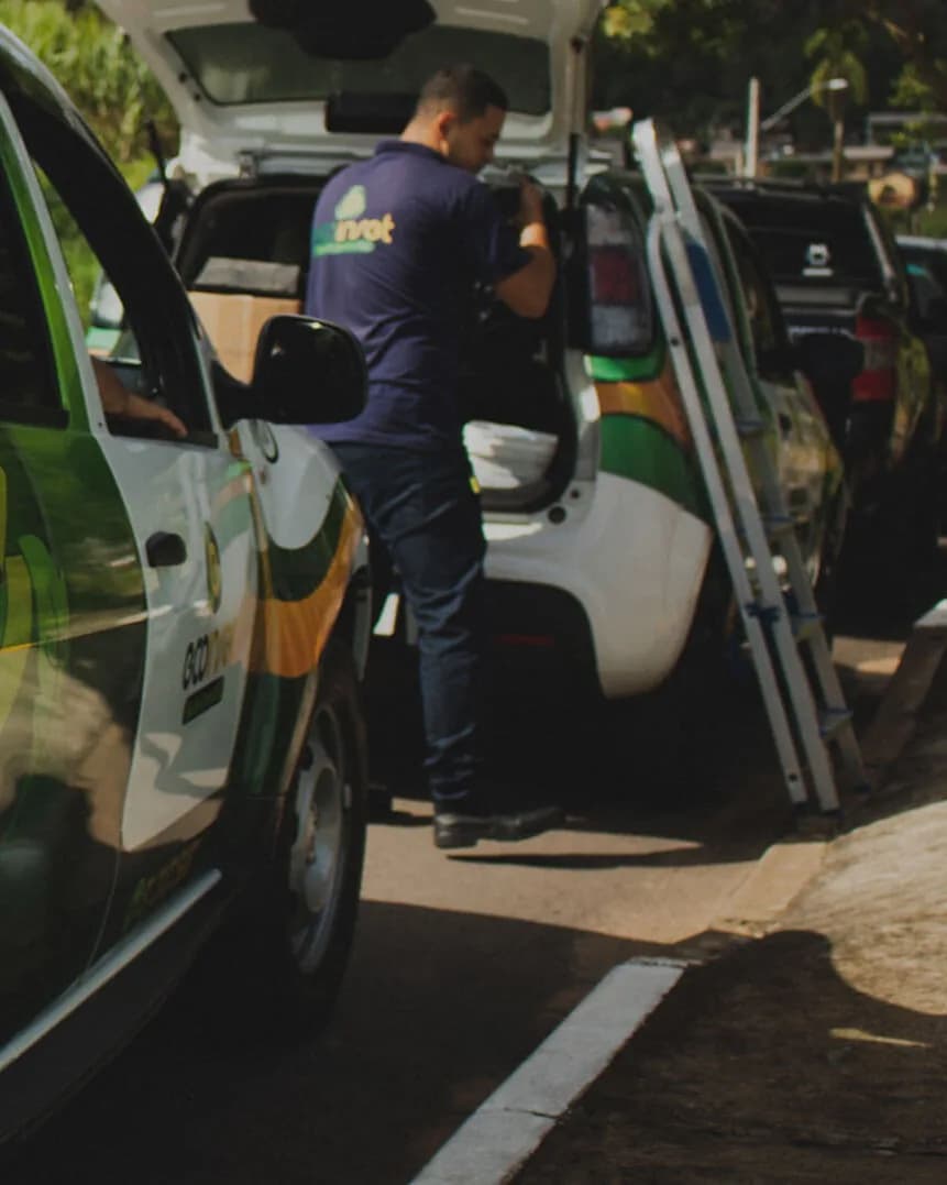 Técnico da Ecoinset, de uniforme azul-marinho com o logo nas costas, prepara o atendimento junto aos carros da empresa.